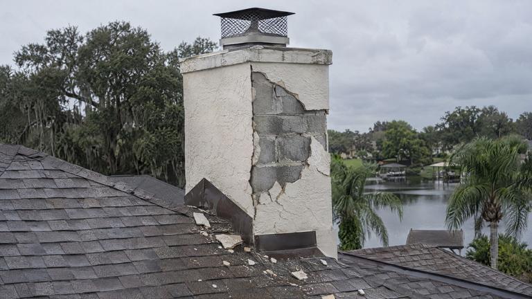 A stucco chimney with cracked stucco fallen away, exposing the concrete block underneath.