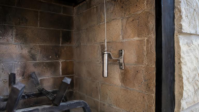The release handle and cable of a top-sealing damper mounted inside a clean brick firebox.