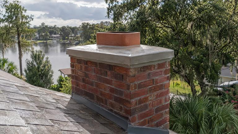 A newly formed concrete crown with an overhang and drip edge on a red brick chimney after rain.