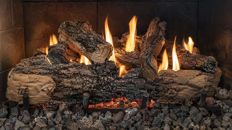 Close view of ceramic gas logs over lava rock, with glowing embers and calm flames.